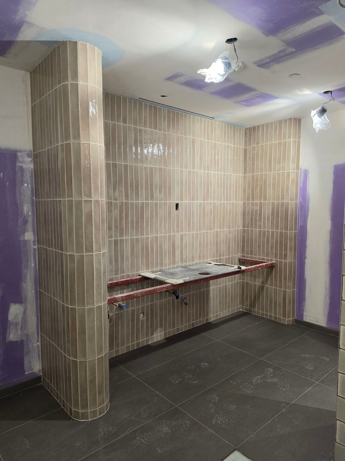 Finished vanity wall and curved column in vertical-stack tile, dark porcelain floor