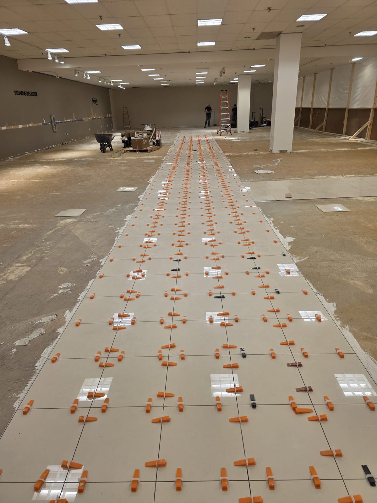 Long run of polished porcelain aisle tiles with leveling clips, walls protected with plastic
